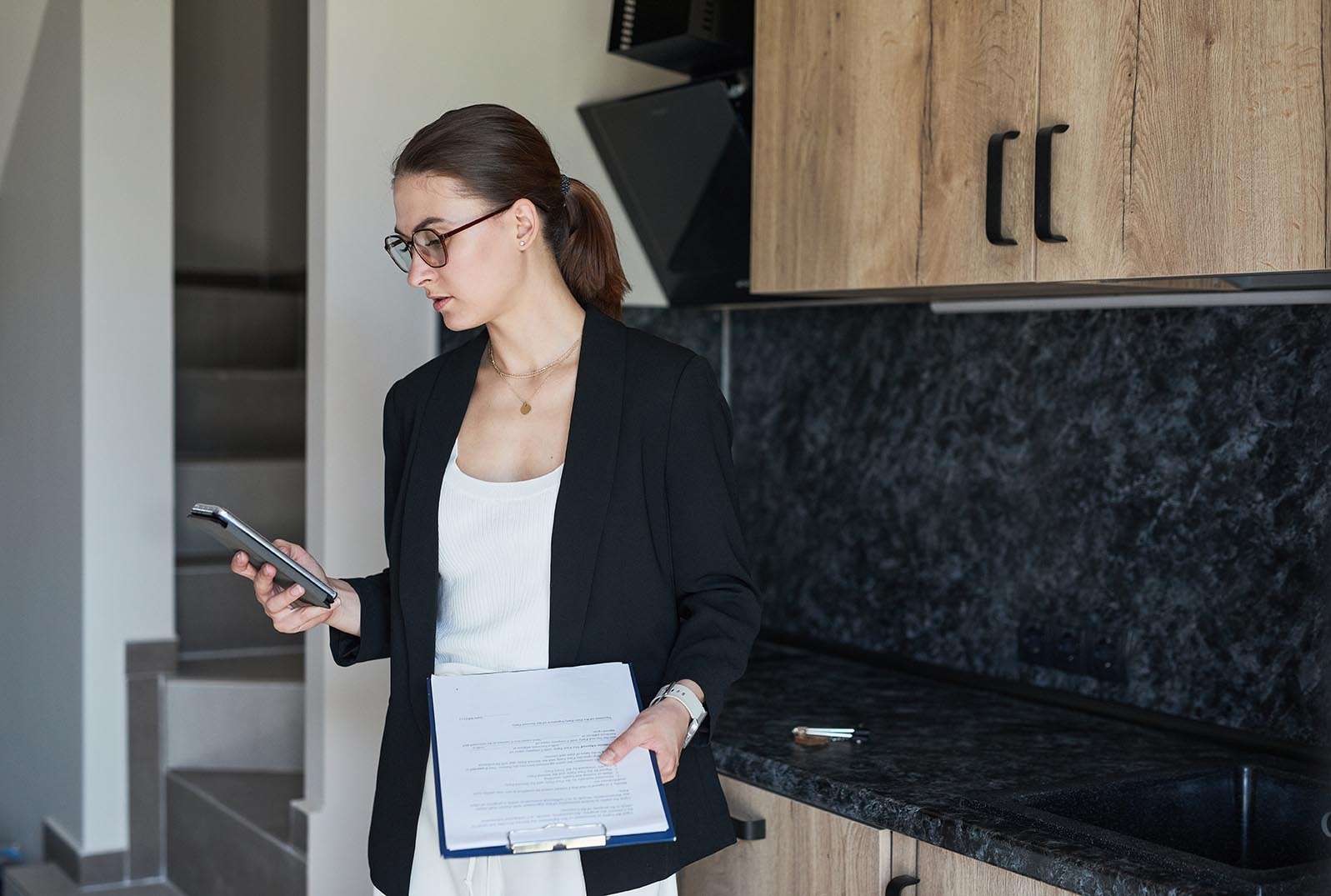 Graphic portrait of female real estate agent using smartphone while standing by kitchen in house for sale, copy space